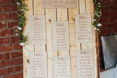 A decor detail shot of a table plan. With cards for each table. Teh plan is on our easel and there are flowers decorating the edge of the frame