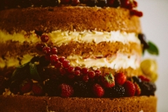 This i a close up shot of a naked spnge cake. You can see 4 layers and between the layers there is cream. There are lots of berries decorating the cake.
