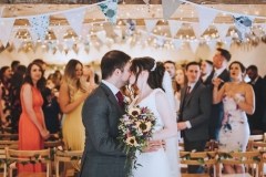 Amy and Kieran  kissing at the entrance to the weding barn with their guests cheering in the background