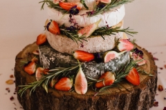 TA close up shot of a "cake of cheese' on a log slice decorated with rosemary and figs.